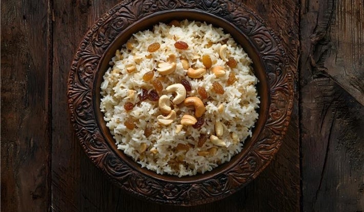 Em cima de uma mesa, um prato redondo com arroz soltinho,uvas-passas e castanhas.