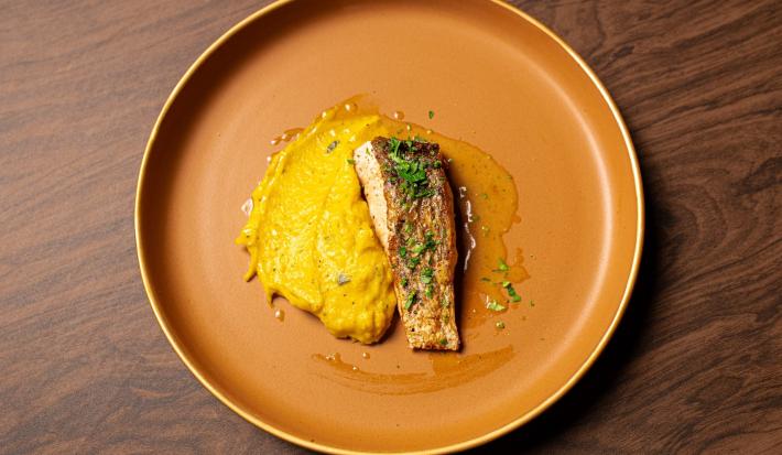Foto da Receita de Robalo com Azeite de Ervas e Purê de Abóbora do Masterchef 11. Observa-se uma foto de cima do prato com o purê bem amarelo à esquerda, servido com o peixe finalizado com salsinha.