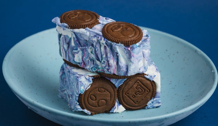 Cubos de sobremesa com creme marmorizado azul e branco e biscoitos de chocolate, servidos em prato azul.