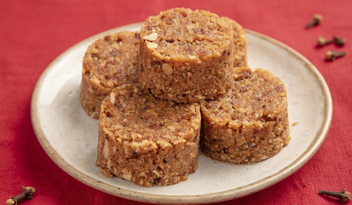Cocadas cremosas em formato cilíndrico, com textura de coco e café, dispostas em prato sobre mesa vermelha.