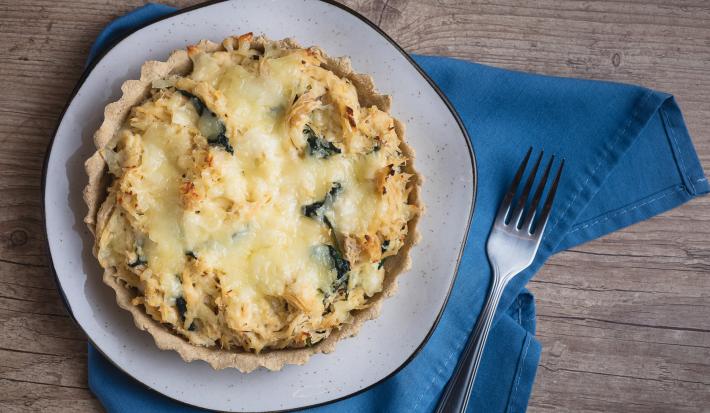 Foto da receita de quiche de aveia com espinafre vista de cima sobre um pano azul com um garfo prateado ao lado direito