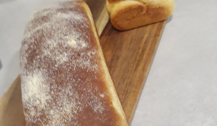 Fotografia de dois pães grandes de milho sobre uma tábua retangular de madeira.