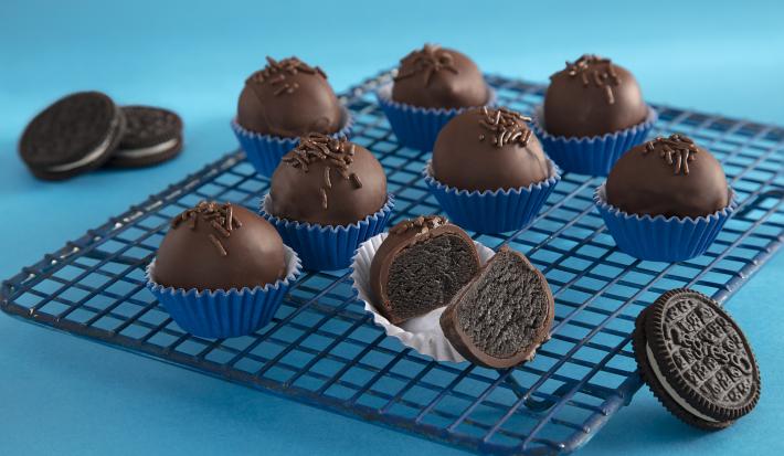Foto da receita de Negresco Trufado. Observa-se uma grade em um fundo azul claro com 8 trufas dispostas em forminhas azuis escuras. A da frente está cortada no meio para mostrar o interior
