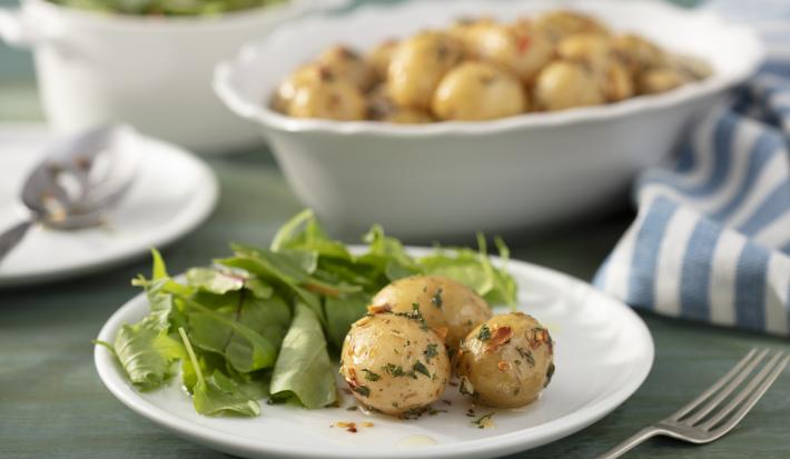 Imagem de um prato com batata calabresa e uma salada verde ao lado. Ao fundo, uma travessa com batatas.