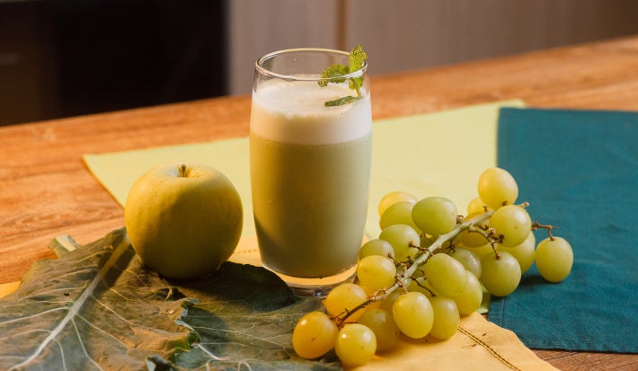 imagem mostra um copo de suco verde cremoso, servido gelado e decorado com folhas de hortelã