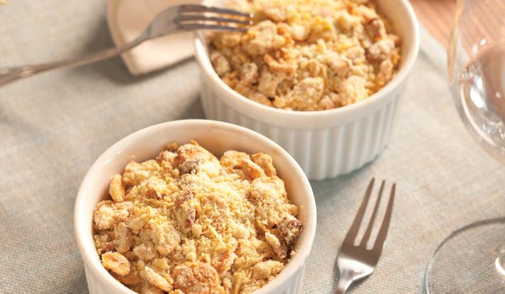 fotografia em tons de cinza, branco e bege de uma bancada cinza vista de cima, contém dois potes redondos e brancos com Crumble de Legumes e queijo ralado por cima, ao lado um garfo para servir.