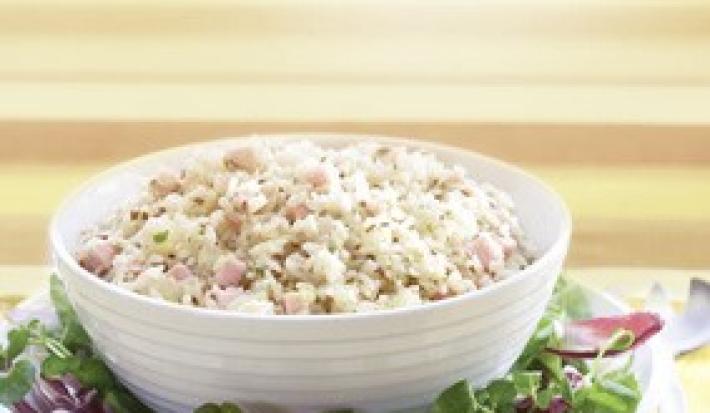 Fotografia em tons de amarelo em uma bancada de madeira clara, um pano amarelo, um prato redondo com salada de alface e cebola roxa e um potinho branco com a salada de arroz dentro dele.