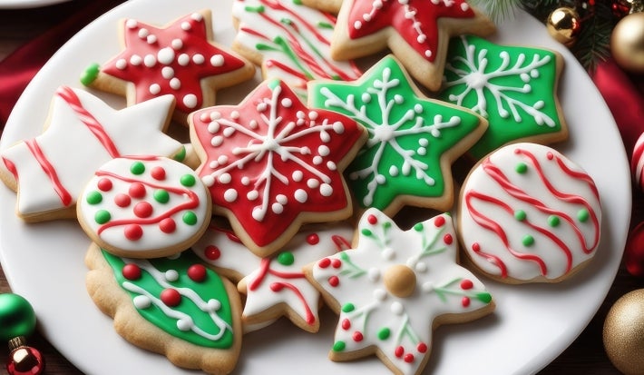 Em cima de uma mesa, prato branco com biscoitos em formato de estrelas e círculos, decorados com glacê colorido e confeitos coloridos.