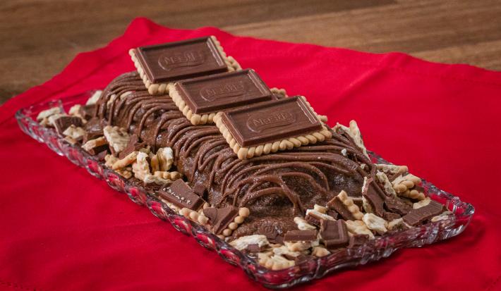 Fotografia de uma torta gelada de chocolate com chocolate derretido e alguns chocobiscuit por cima e ao lado.