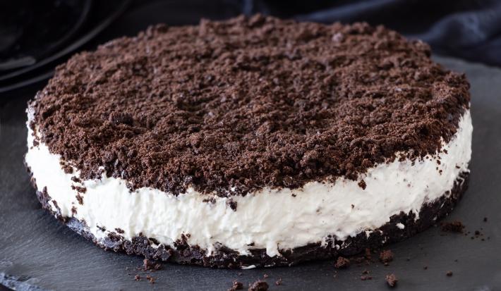 Fotografia de um sanduíche com base e topo de biscoito de chocolate triturado, recheado com creme branco.