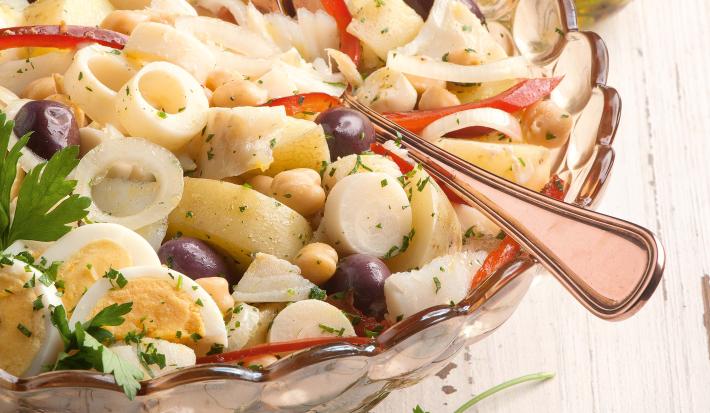 Fotografia em tons de branco de uma bancada de madeira branca com um recipiente de vidro com bacalhau. Ao lado um recipiente de vidro com azeite.