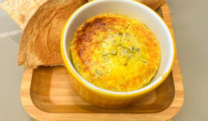 Fotografia em tons de amarelo com um ramekin amarelo ao centro. Dentro dele existe uma receita de ovos cremosos acompanhado de pão.