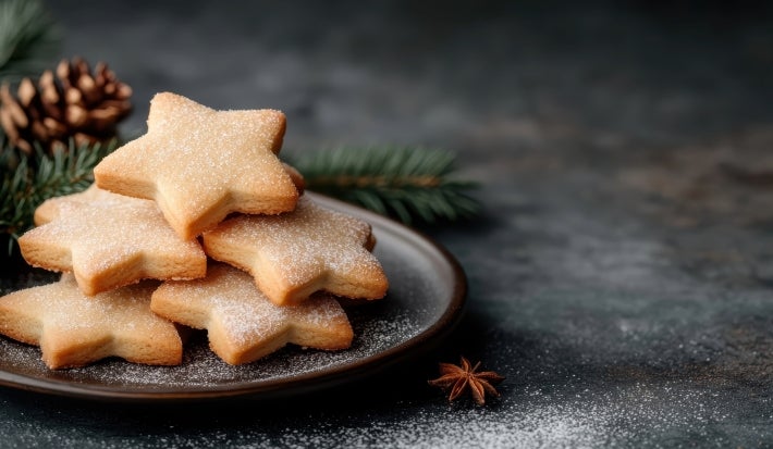 Em cima de uma mesa, prato redondo com biscoitos em formato de estrelas, decorados com açúcar de confeiteiro.