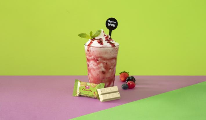 Foto em tons de cor de rosa e verde da receita de smoothie iogurte servida em um copo alto sobre uma mesa cor de rosa com um kit kat hortelã à frente