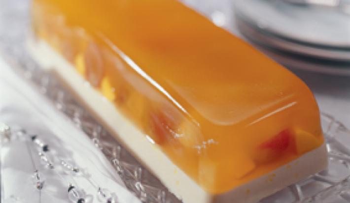 fotografia em tons de branco e laranja contém uma sobremesa gelada com camada de gelatina de frutas e pedaços de frutas.