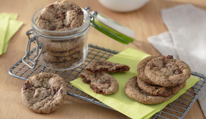 Foto da receita de Cookies Sem Glúten. Observa-se um pote hermético de vidro com os cookies dentro sobre uma grade. Ao lado direito, cookies dispostos sobre um guardanapo verde.