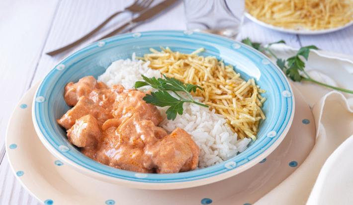 Imagem de um prato azul claro com strogonoff de frango, arroz branco e batata palha decorado com uma folha de salsa.