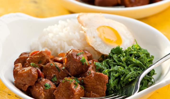 fotografia vista de frente, contém dois recipiente branco e redondo e ambos contém: arroz, couve, pedaços de carne e ovo com um garfo para servir
