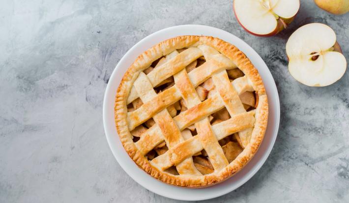 Imagem vista de cima de um prato branco com uma torta de maçã trançada com dois pedaços de maçãs cortadas ao meio.