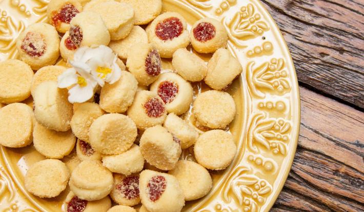 Fotografia de um prato amarelo de vidro sobre uma mesa de madeira. Dentro do prato tem várias unidades de biscoitos amanteigados com goiabada.