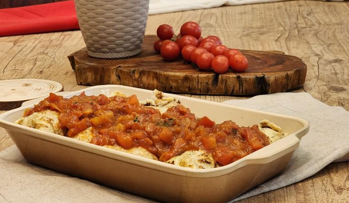 Fotografia em tons de marrom com uma travessa funda ao centro. Dentro da travessa existe algumas panquecas recheadas de carne cobertas com molho de tomate. Ao fundo existe um ramo de tomate cereja.