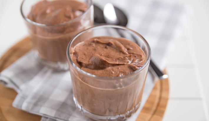 Receita de Mousse de Chocolate da Tia Alzira, tradicional e prático, feito com Chocolate Meio Amargo NESTLÉ CLASSIC, NESTLÉ Creme de Leite e claras em neve, servido em copinhos sobre uma mesa com uma tábua de madeira e colheres ao fundo
