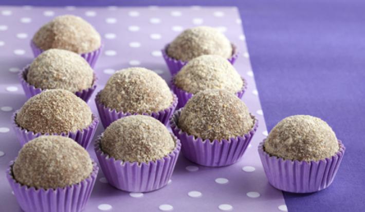 Fotografia em tons de roxo em uma mesa com uma toalha roxa escura, um paninho lilás com bolinhas brancas e vários brigadeiros de cookie dentro de forminhas de docinhos roxa.