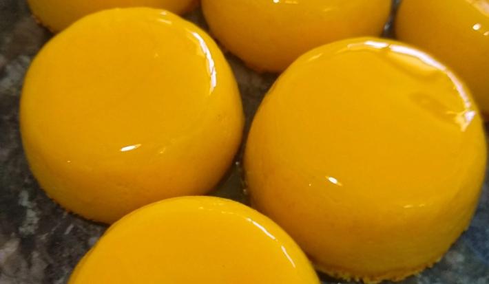 Foto da receita de Quindim. Observa-se quindins bem brilhosos e amarelinhos em uma superfície.