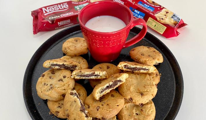 Fotografia de um prato preto servido de cookies e uma xícara vermelha com leite dentro.