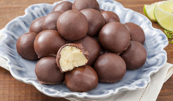 Fotografia em tons de marrom e azul de uma bancada de marrom com um paninho branco, sobre ele um prato azul com trufas. Ao fundo fatias de limão.