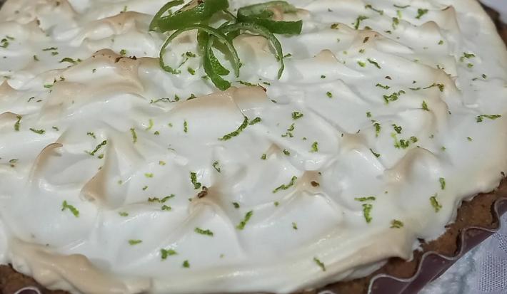 Foto da receita de Torta de Limão. Observa-se uma Torta de Limão grande e inteira com merengue queimadinho e raspas de limão por cima decorando