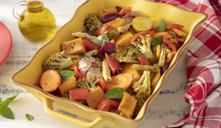 Foto da receita de Panaché de Legumes. Observa-se um refratário amarelo com os legumes cozidos. Ao lado esquerdo, um pote de vidro com azeite e, do direito, uma toalha quadriculada vermelha