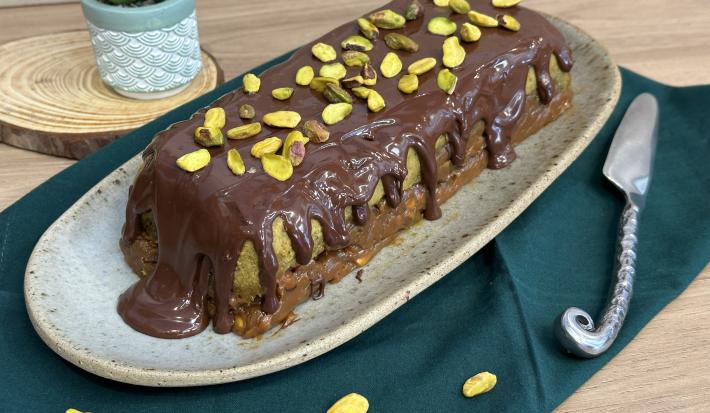 Fotografia de uma sobremesa de cores verde, caramelo e chocolate coberta com chocolate derretido e pistache