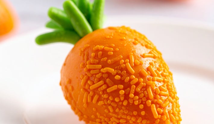 Fotografia mostra brigadeiro em formato de cenoura sobre um prato raso branco.