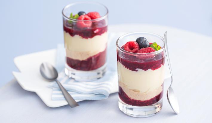 fotografia em tons de branco e vermelho tirada de dois copos transparentes com geleia de frutas vermelhas e leite MOÇA de colher com frutas vermelhas por cima e colheres ao lado.