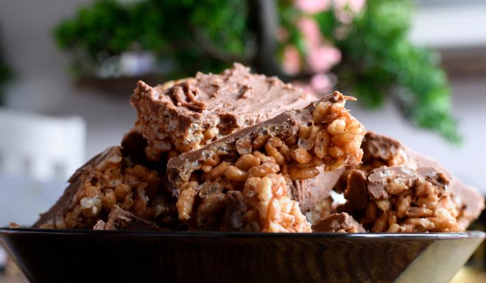 Fotografia de alguns docinhos com cobertura de Chocolate ao Leite GAROTO com crespinho de arroz dentro de um recipiente preto fundo.