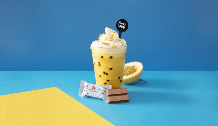 Foto em tons de azul da receita de smoothie de maracujá servida sobre uma mesa azul com um kit kat de menta à frente