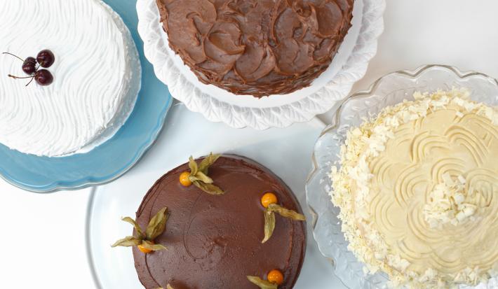 4 bolos com diferentes sabores por cima de pratos onde 2 são de vidros um é branco e o outro azul.