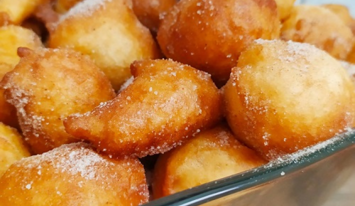 Foto da receita de Bolinho de chuva sem ovo. Observa-se um refratário quadrado de vidro transparente com os bolinhos fritos e polvilhados de açúcar dentro.