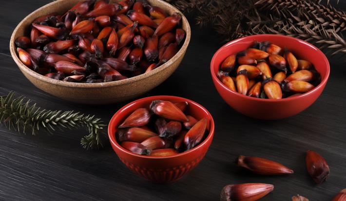 Fotografia em tons escuros com 3 potes ao centro. Em cima de cada pote existe uma receita de pinhão cozido que foi feito na airfryer.