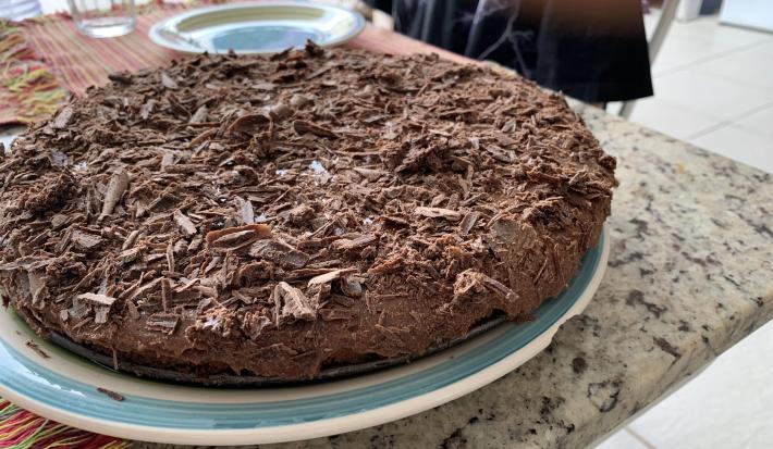 Fotografia de uma torta de chocolate com raspas de chocolate sobre um apoio branco com borda azul.