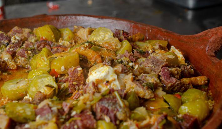 Fotografia de uma frigideira grande de barro com uma receita de maxixe e carn seca.