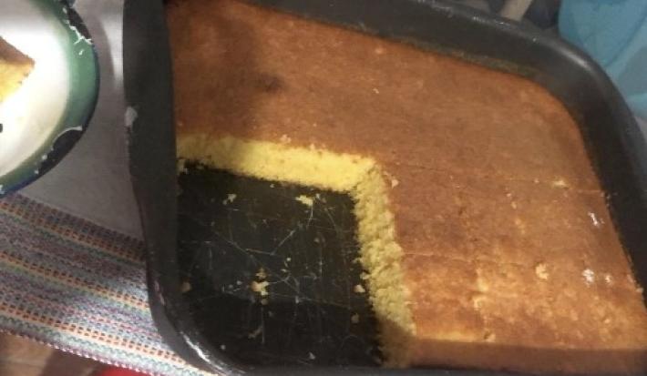 Fotografia de uma forma retangular preta grande com bolo de flocão de milho. Nota-se que faltam quatro pedaços no bolo na forma.