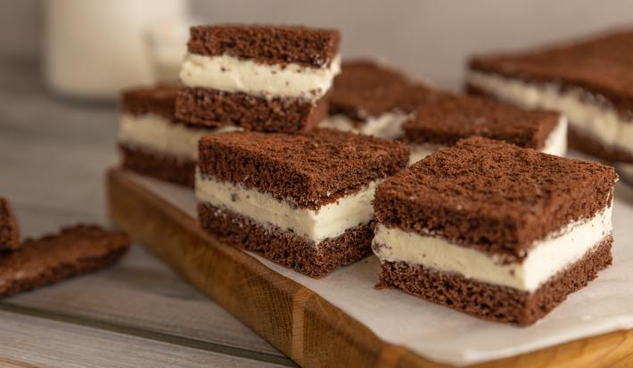 Fotografia de pedaços quadrados de bolo de chocolate recheado com creme de limão, e estão sobre um papel manteiga, apoiado em uma tábua de madeira.