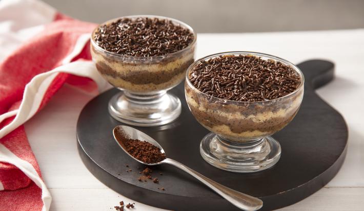 Foto da receita de Bolo de Brigadeiro de Café no Potinho. Observa-se dois potinhos transparentes intercalando uma camada de bolo branco e uma camada de brigadeiro de café. No topo, granulados para decorar.