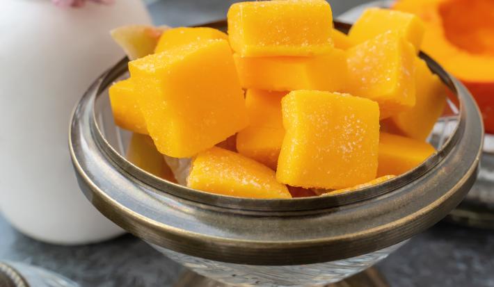 Fotografia em tons de amarelo com um recipiente de vidro ao centro. Dentro do recipiente existe várias balas pequenas de gelatina feitas com FiberMais Laranja.