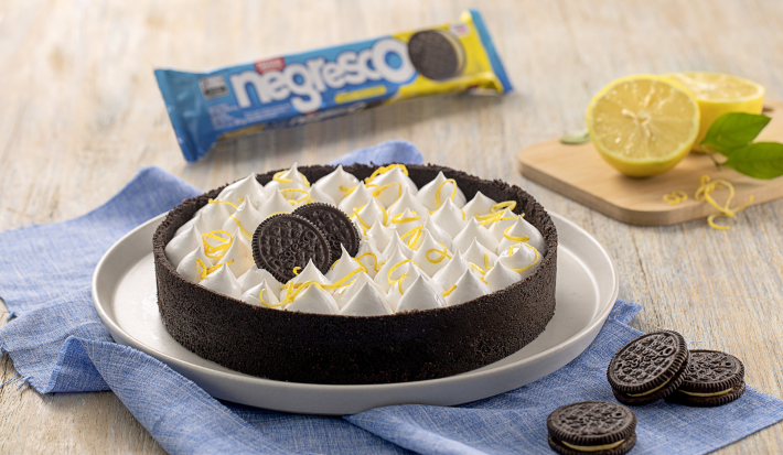 Fotografia mostra uma de torta de limão siciliano com a massa escura feita com biscoito, em cima um merengue com raspas de limão amarelo.