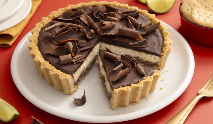 Foto da receita de Torta de Limão com Chocolate. Observa-se uma torta com cobertura de ganache e raspas de chocolate com um pedaço fatiado.