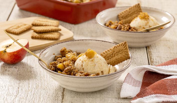 Fotografia em tons de marrom claro com um prato fundo ao centro. Dentro do prato existe um crumble feito com biscoito TOSTINES com maçã acompanhado de sorvete de creme.