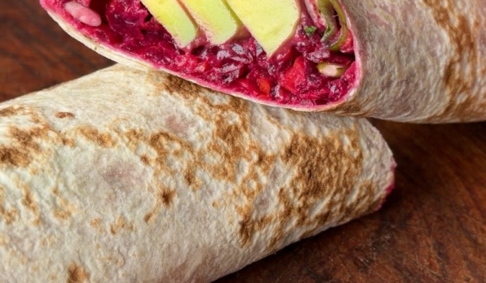Fotografia em tons de marrom e vermelho de um wrap recheado de beterraba e cenoura.